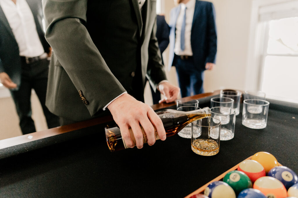 Groom pouring a drink of whiskey for his friends before his winter wedding.