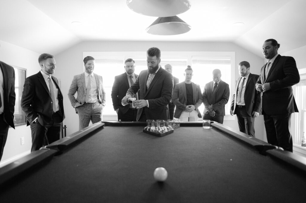 Groom pouring a drink of whiskey for his friends before his winter wedding.